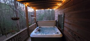 Un jacuzzi en una terraza de madera con barandilla, rodeado de árboles.