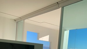 A modern bedroom with a large bed, a TV, and a view of the sea through large windows.