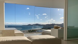 A modern living room with a large glass door leading to a balcony overlooking a beach and ocean.