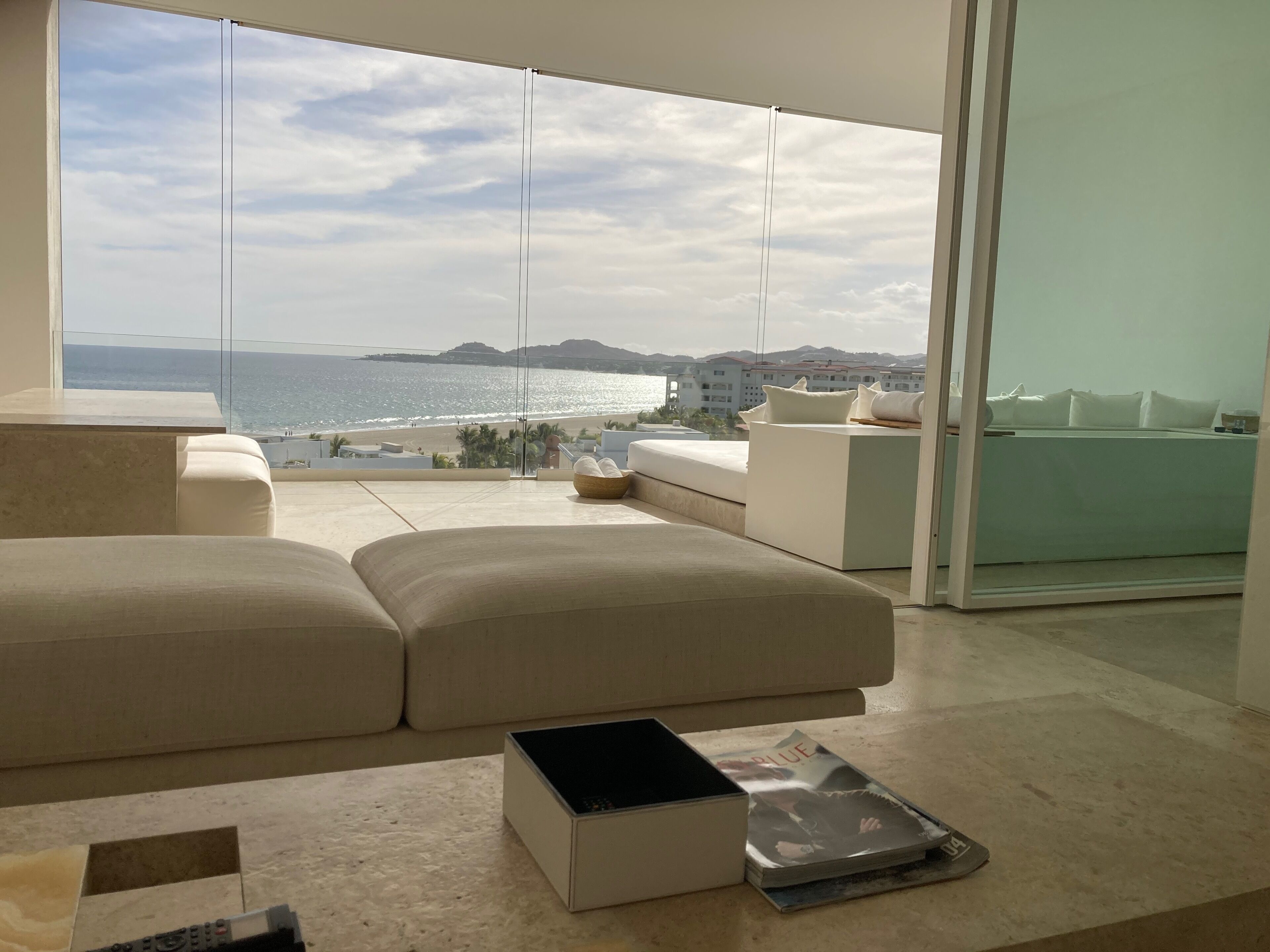Een moderne woonkamer met een groot raam met uitzicht op een strand en stadsbeeld.