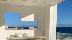 A modern spa area with a large bathtub, white furnishings, and a view of the ocean.