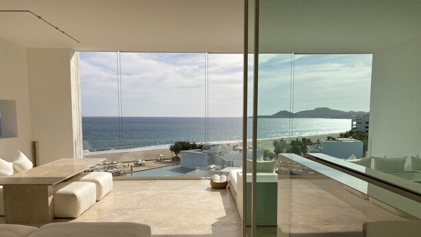 A modern interior with a large glass wall offering a view of the beach and ocean.