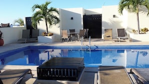 A swimming pool with lounge chairs and a table, surrounded by white walls and palm trees. - Luxury Penthouse with 2 BR - Meridian (Playa del Carmen)