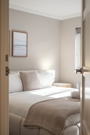 Ein Schlafzimmer mit Bett, Kissen, einem Nachttisch, einer Lampe und einem gerahmten Bild an der Wand.