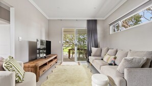 Una sala moderna con un televisor de pantalla plana sobre un soporte de madera, un sofá beige con almohadones, un sillón a rayas y una alfombra grande.