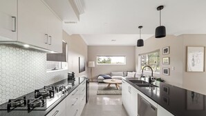 A modern kitchen with a hexagonal backsplash, a central island, and a dining area with a sofa and coffee table. - Station Stays | Margaret River NEW (Margaret River)