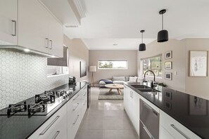 A modern kitchen with a hexagonal backsplash, a central island, and a dining area with a sofa and coffee table. - Station Stays | Margaret River NEW (Margaret River)