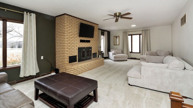 A living room with a brick fireplace, a ceiling fan, and a large window. - Nicely Located 2-bedroom duplex apartment newly updated in Herington. (Herington)
