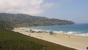 A coastal beach with a lifeguard tower, sandy shore, and a hillside with buildings.