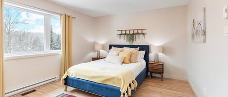 A bedroom with a bed, bedside tables, a hanging plant, and a window with curtains.