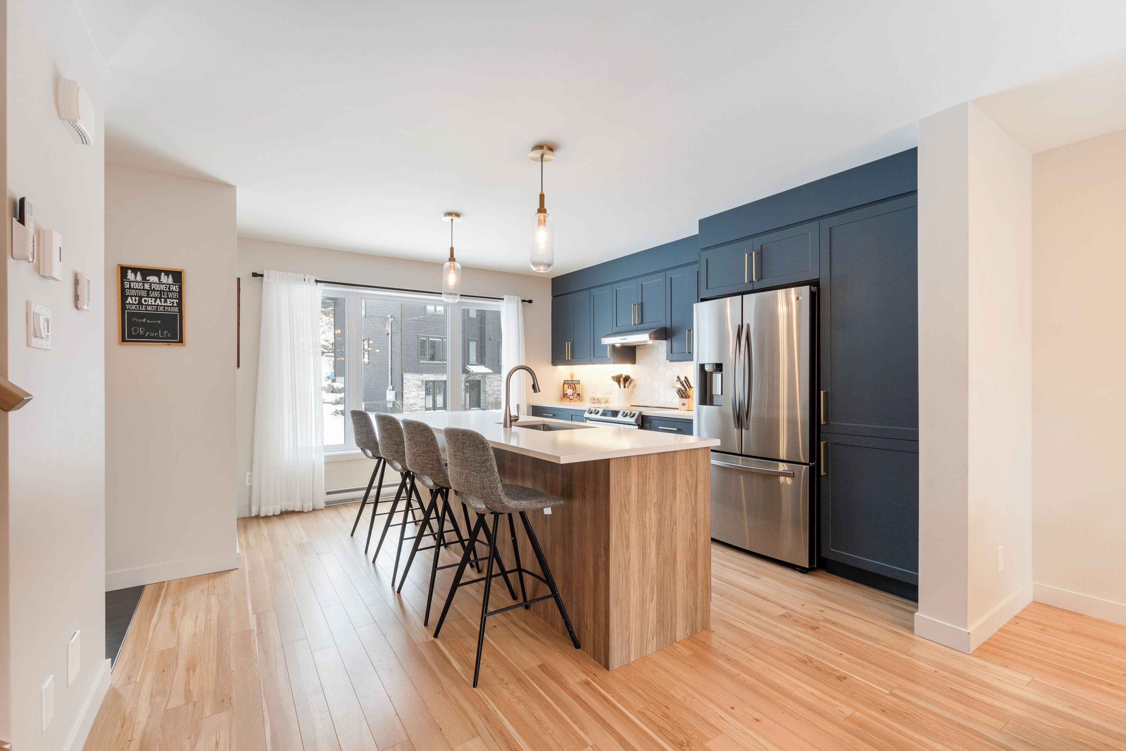 A modern kitchen with a central island, bar stools, stainless steel appliances, and a view to the outside.