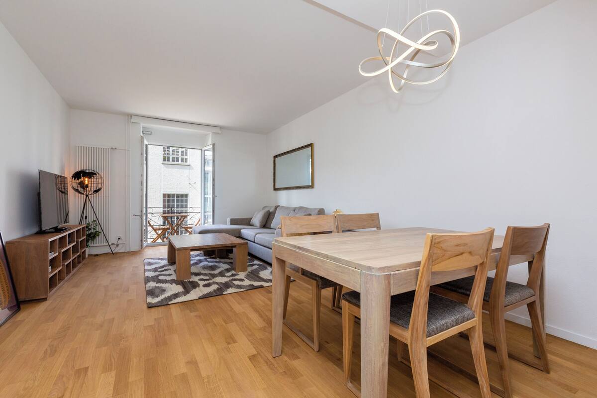Ein modernes Wohnzimmer mit einem Holzesstisch, Stühlen, einer Couch und einem Fernseher.