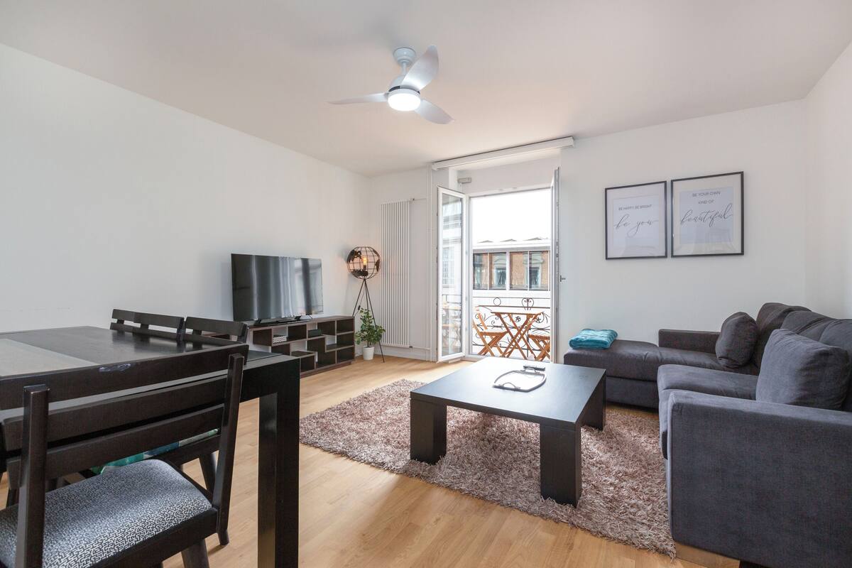 Ein modernes Wohnzimmer mit Essbereich, einem grauen Sofa, einem Couchtisch und einem Fernseher.