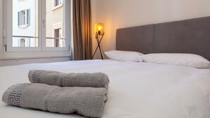 A hotel room with a bed, pillows, a nightstand with a lamp, and a window with curtains. - KAYA Zurich Elisabethenstrasse (Zürich)