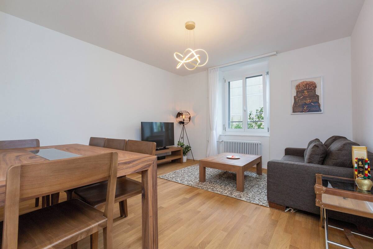 Ein modernes Wohnzimmer mit einem Holzesstisch, einer Couch, einem Fernseher und einer Stehlampe.