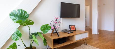 A modern living room with a wooden TV stand, a flat-screen TV, a potted plant, and a framed picture.