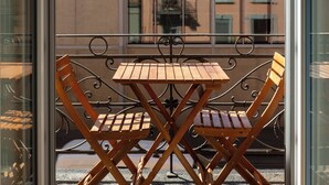 A balcony with a wooden table and chairs, a view of a building with multiple windows, and a clear sky. - KAYA Zurich Elisabethenstrasse (Zürich)
