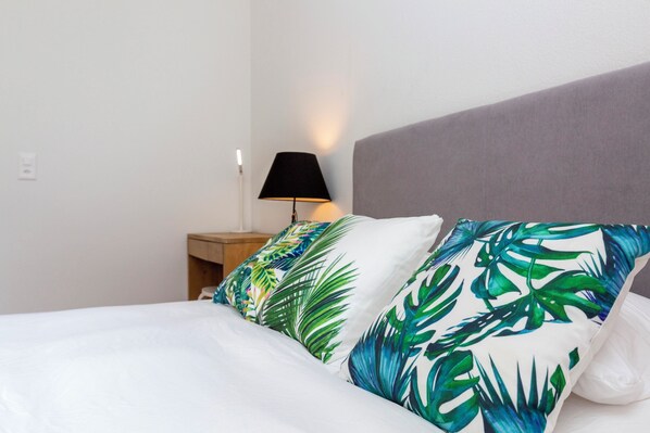 Un lit avec une literie blanche et deux oreillers ornés d’un motif de feuilles tropicales.