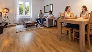 A living room with a wooden floor, a dining table with chairs, a sofa, and a lamp. - KAYA Zurich Elisabethenstrasse (Zürich)