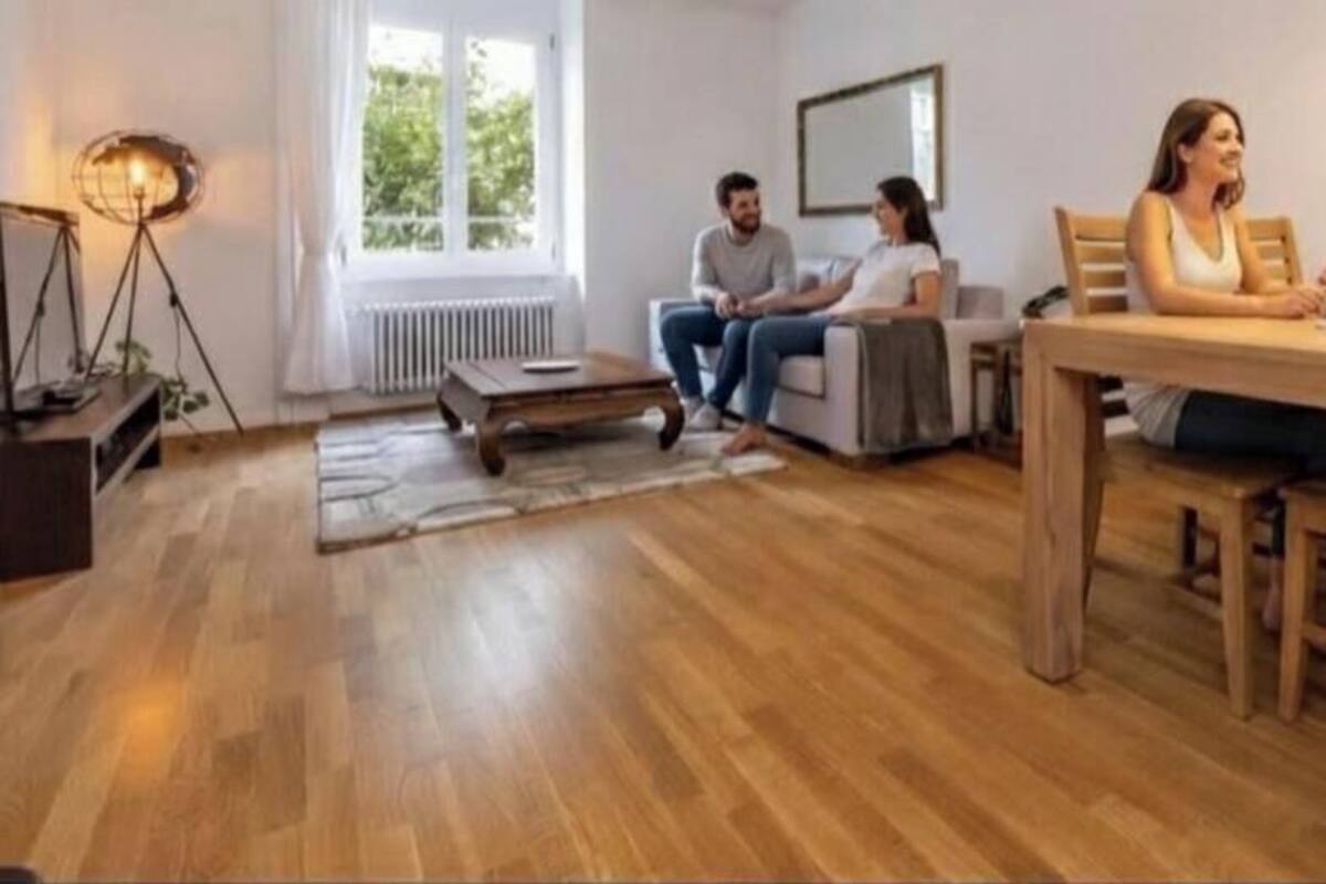 Ein Wohnzimmer mit Holzboden, einem Esstisch mit Stühlen, einer Couch und einer Lampe.