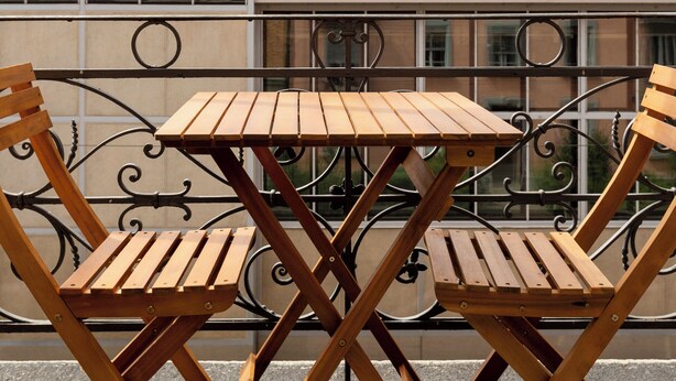 A wooden table and chairs on a balcony with a wrought iron railing, overlooking a cityscape with buildings and a mountain in the background. - KAYA Zurich Elisabethenstrasse (Zürich)