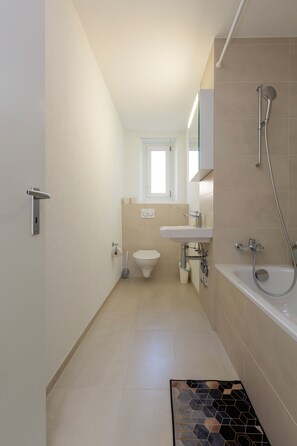 Bathroom features a white toilet, sink, and bathtub with showerhead, set against a light-colored backdrop.