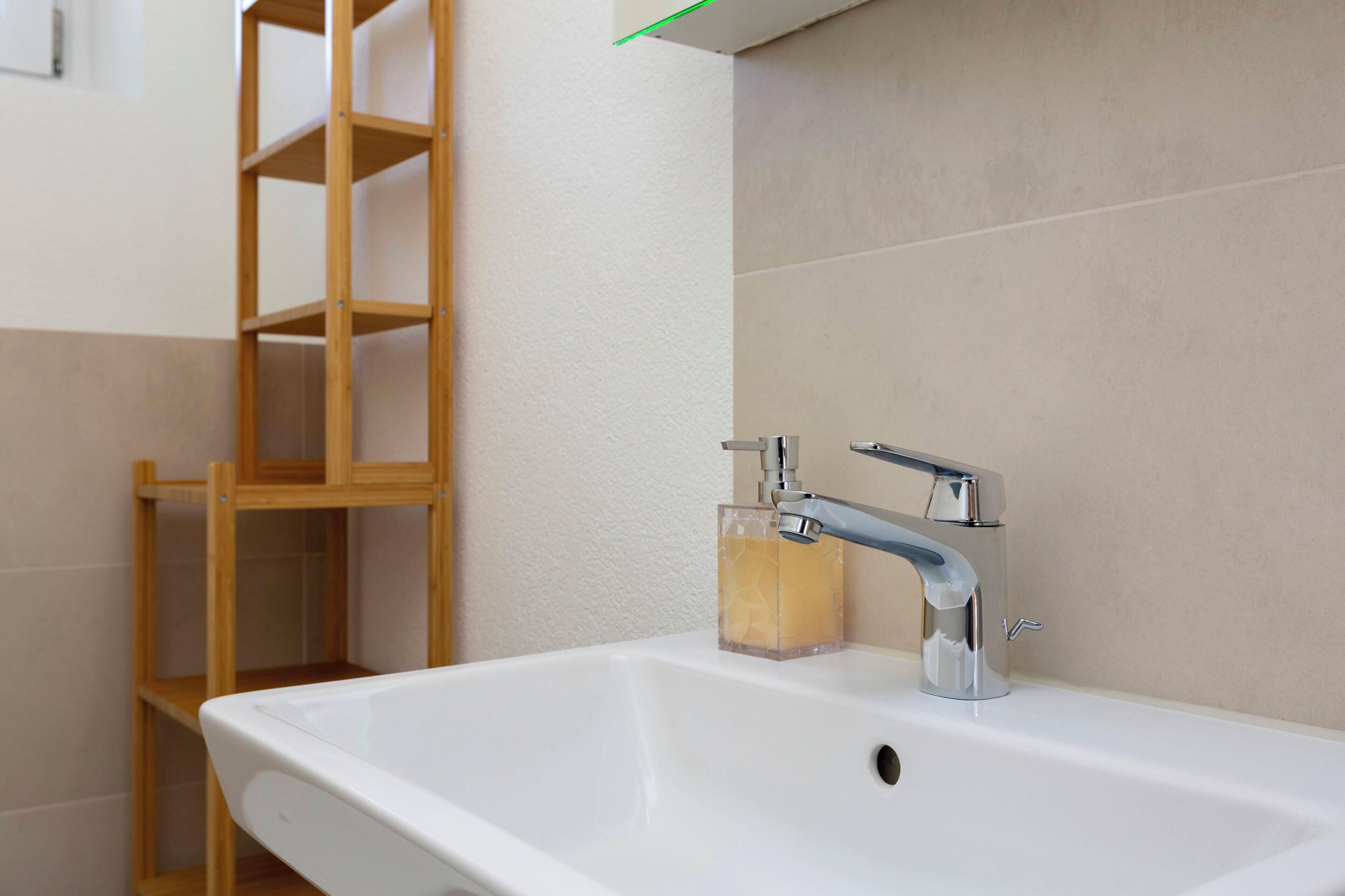 A bathroom with a white sink, a chrome faucet, and a wooden shelf.