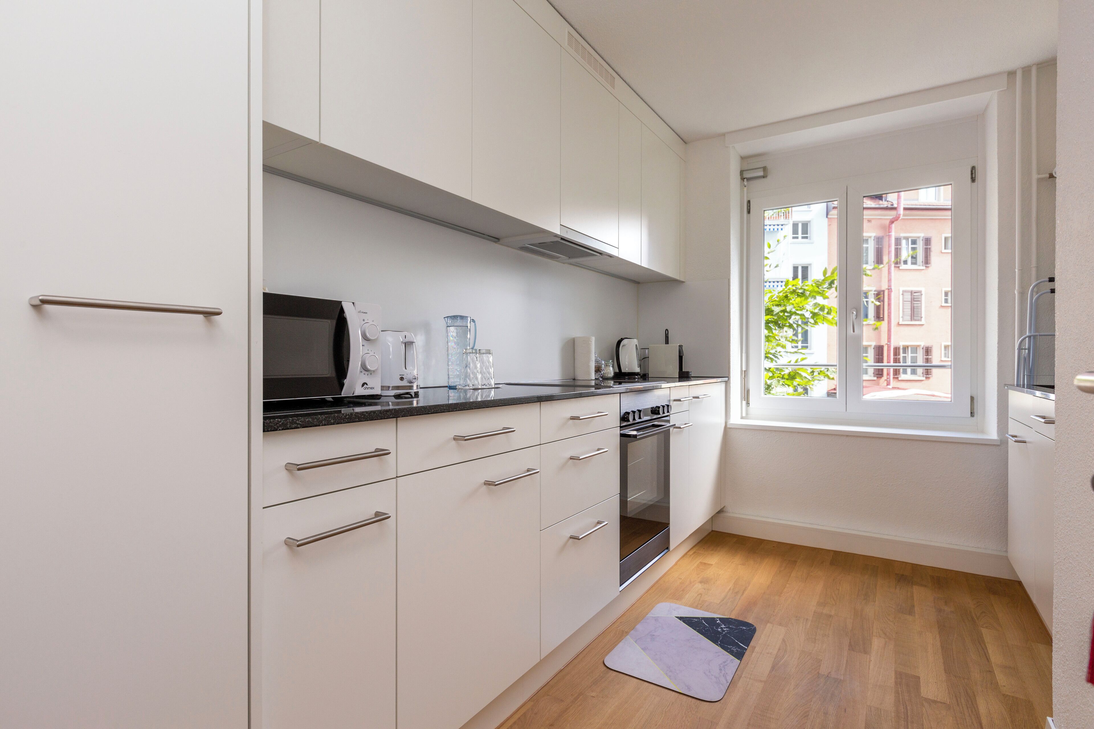 A modern kitchen with white cabinets, a black countertop, and a window with a view of buildings.