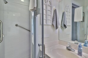 Bathroom features a glass shower enclosure, handrail, and large mirror with decorative window design.