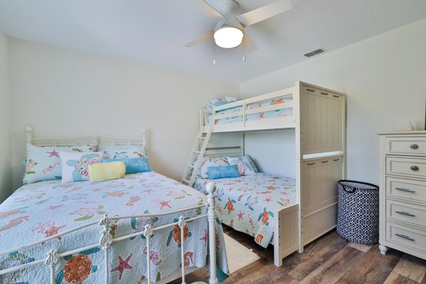 A bedroom with bunk beds, a ceiling fan, a dresser, and a trash can. - 4/3 pool home steps from the ocean! (New Smyrna Beach)