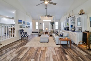 A spacious living room with hardwood flooring, a ceiling fan, a large window, and a white kitchen with white cabinets and a wooden countertop. - 4/3 pool home steps from the ocean! (New Smyrna Beach)