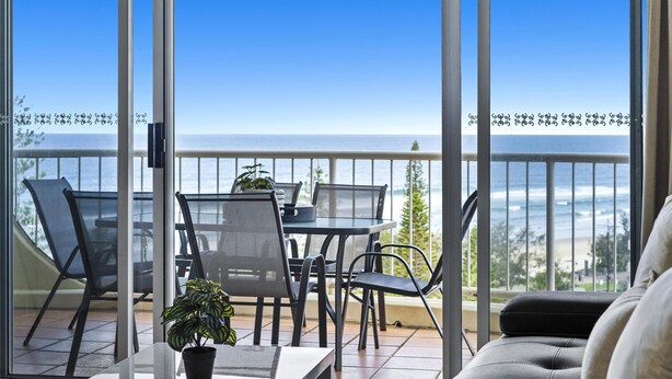 Een balkon met uitzicht op de oceaan, voorzien van een tafel, stoelen en een bloempot.