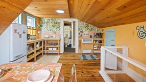 A cozy kitchen with wooden beams, a refrigerator, a dining table with plates, and a colorful wall.