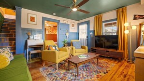 A cozy living room with a blue accent wall, a ceiling fan, a large flat-screen TV, and a colorful rug.