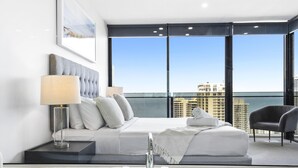 A modern hotel room with a large bed, a sitting area, a bathtub, and a view of the city through large windows. - 1 Bedroom + Study Ocean View Apartment — Q Stay (COC 1313 - 2N - NB) (Surfers Paradise)