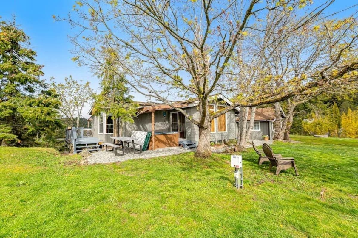 A rustic cabin with a wooden deck, a covered outdoor seating area, and a large tree in front.
