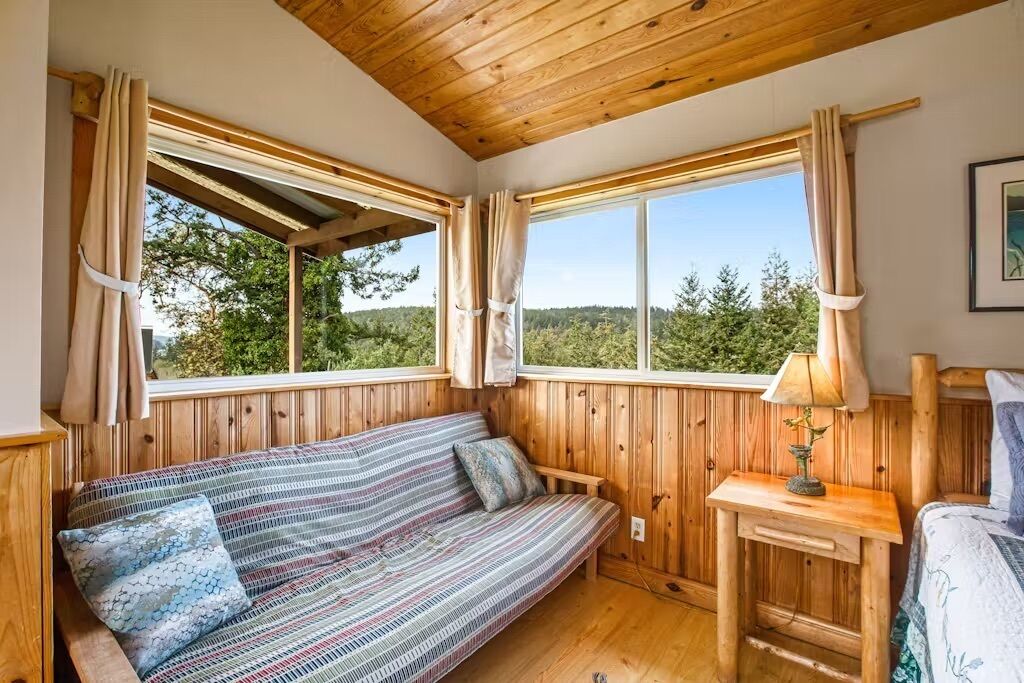 A wooden cabin room with a bed, a sofa, and a window with curtains.