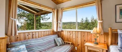 A wooden cabin room with a bed, a sofa, and a window with curtains.