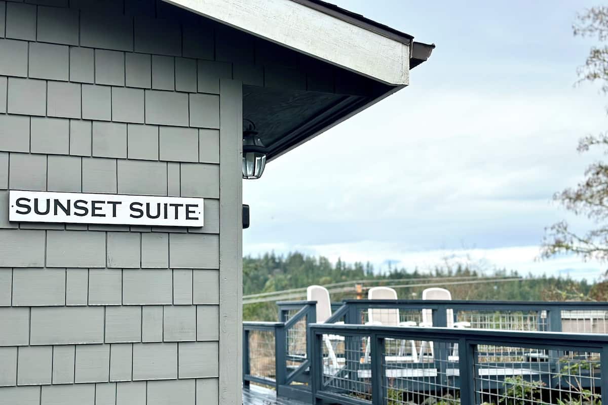 A building with a sign reading "SUNSET SUITE" and a view of a deck with chairs.