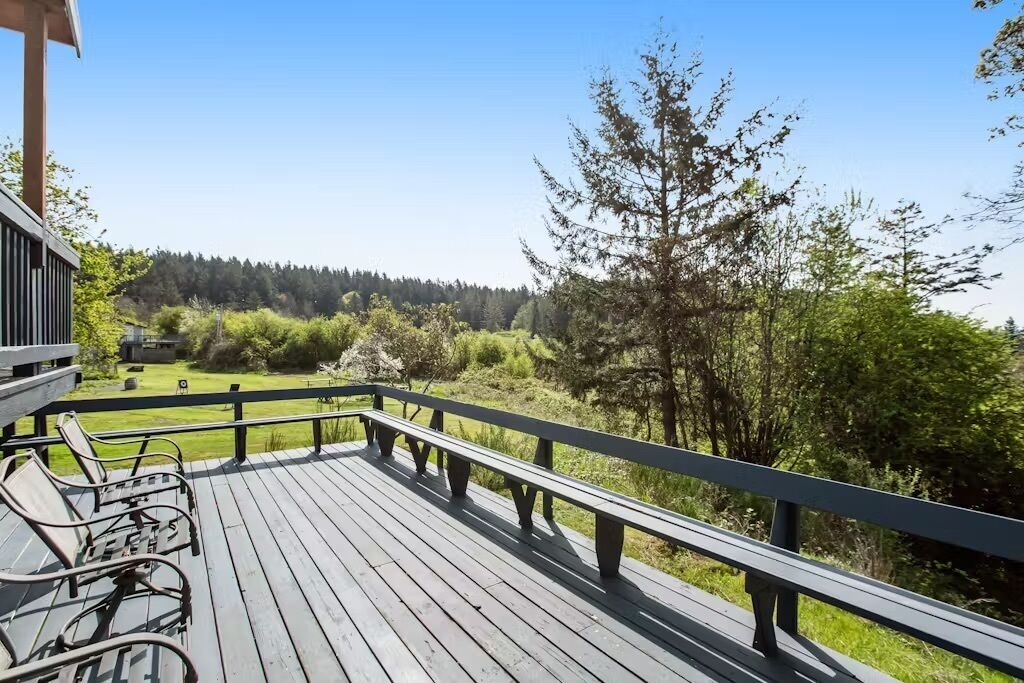 A wooden deck with metal chairs, overlooking a green landscape with trees and a distant view of a building.