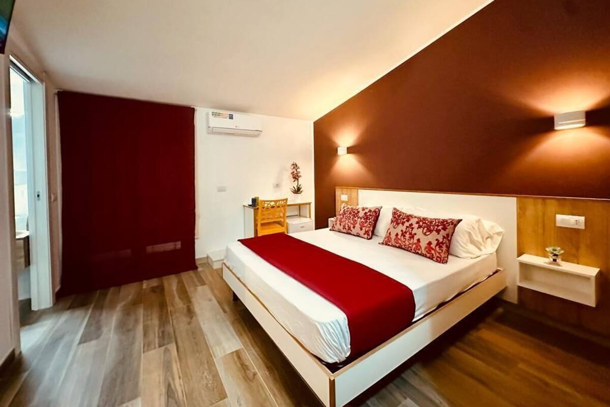 Un dormitorio moderno con una cama grande, suelo de madera, cortina roja, mesita de noche y una lámpara de pared.