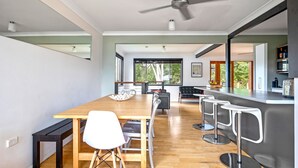 A modern kitchen with a wooden table, bar stools, and a view of the outdoors. - Lightly Salted in Mollymook (Mollymook Beach)