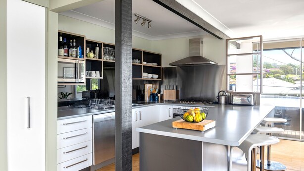A modern kitchen with a central island, stainless steel appliances, and a view of the outdoors through large windows. - Lightly Salted in Mollymook (Mollymook Beach)
