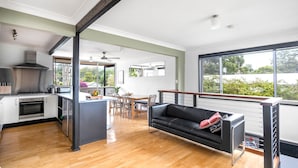 A modern kitchen with a gas stove, oven, and a dining area with a table and chairs. - Lightly Salted in Mollymook (Mollymook Beach)