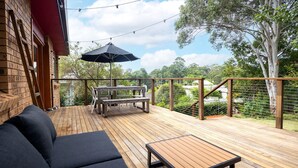 A wooden deck with a table and chairs, a sofa, and a pergola with string lights. - Lightly Salted in Mollymook (Mollymook Beach)