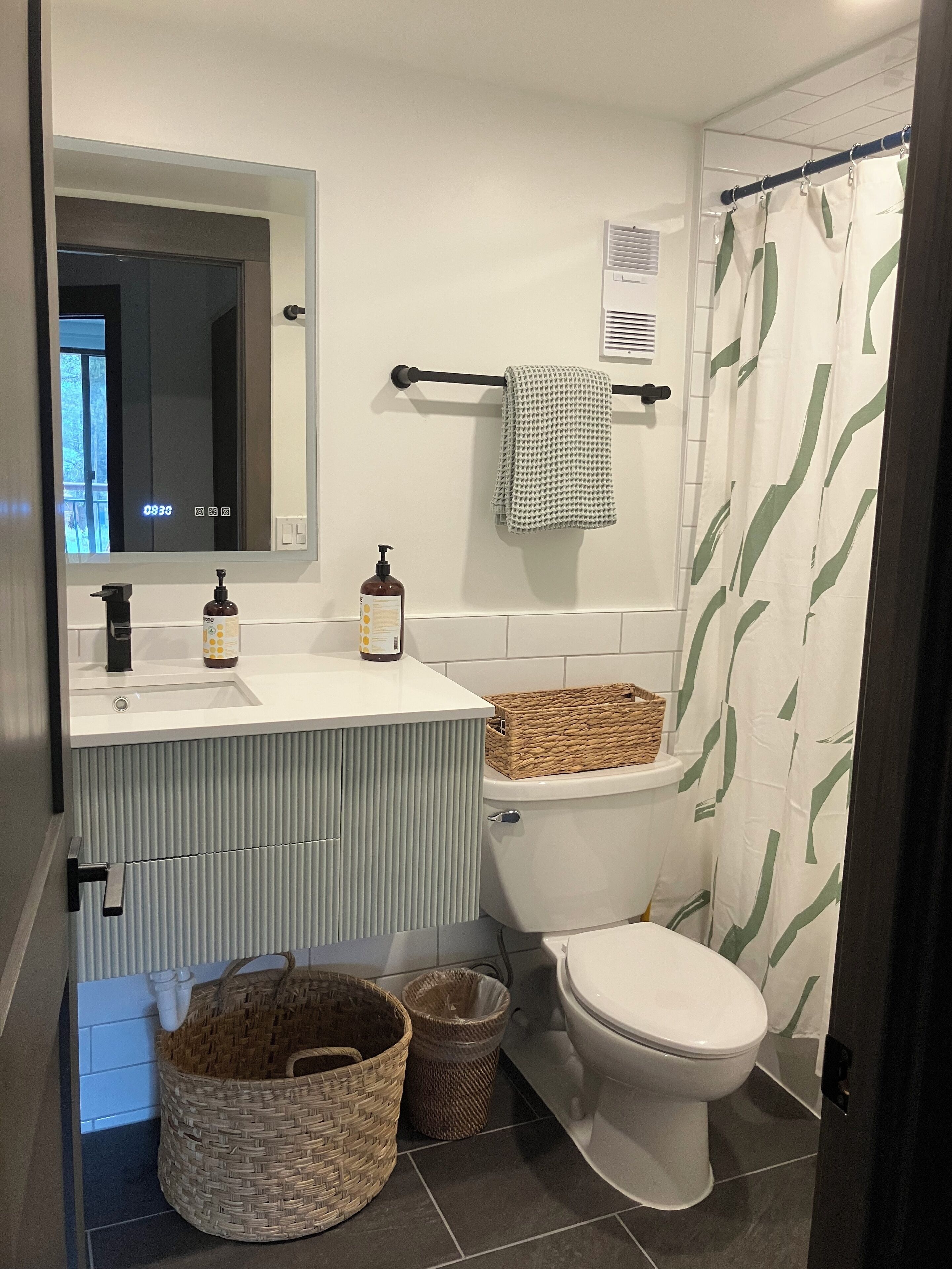 A modern bathroom with a white sink, a mirror, a toilet, and a shower curtain.