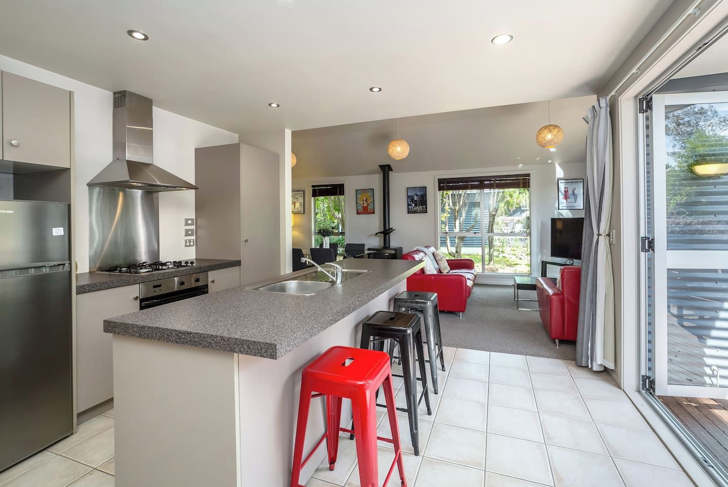 A modern kitchen with a central island, stainless steel appliances, and a dining area with red bar stools.