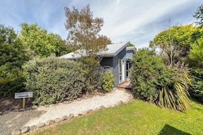 A house with a gravel pathway leading to the entrance, surrounded by dense greenery and trees.