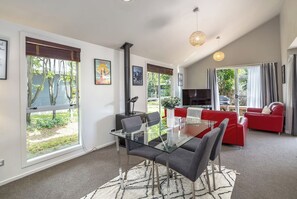 A modern living room with a glass dining table, red sofa, and a TV. - Apartment Sauvignon, Martinborough (Martinborough)