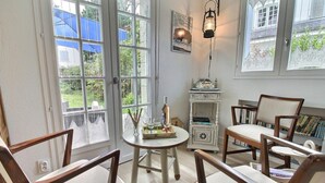 Ein Zimmer mit rundem Tisch, Holzstühlen, einem kleinen weißen Schrank und einem Fenster mit Blick ins Grüne.
